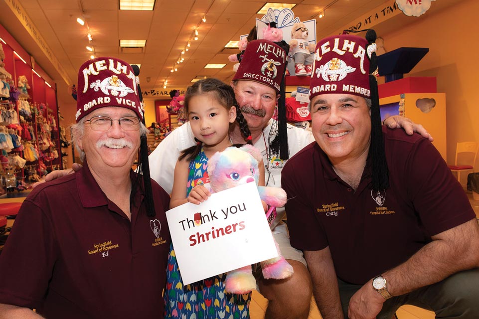 Three Shriners wearing red fezzes with a little girl holding a stuffed animal and sign that says "Thank you Shriners!"